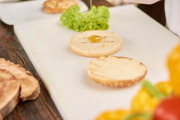 The process of cooking burger at kitchen. Bun for hamburger pouring with sauce. Cooking and culinary concept.