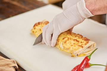 Chef hands cutting burrito on pieces. Cook chopping mexican burrito. Chef at work, cooking.