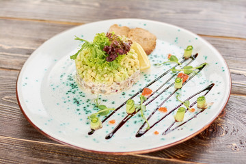 Delicious salad on wooden table. Appetizing salad with herring, avocado and toasts in restaurant. Tasty dinner on plate.