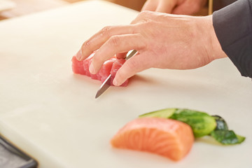 Chef cutting fresh tuna in small pieces. The process of slicing raw tuna fillet by chef. Chef at work, cooking.