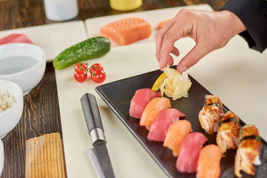 Chef adding ginger to sushi on plate. Cook serving sushi nigiri with ginger. Appetizing sushi in restaurant.