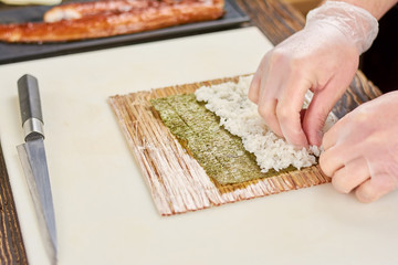 Male cook preparing sushi at restaurant. Chef hands cooking sushi with rice and nori. Process of japanese sushi roll preparation.