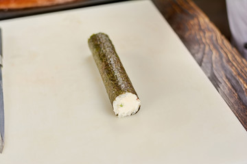Long sushi roll with rice and nori. Sushi preparation at japanese restaurant kitchen. Traditional japanese food.