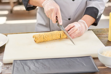 Male hands cutting long sushi roll. Japanese chef cutting sushi roll on white cutting board.