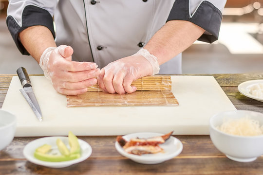Chef hands shaping sushi roll. Male cook hands making japanese sushi roll with bamboo mat. Chef at work, kitchen.