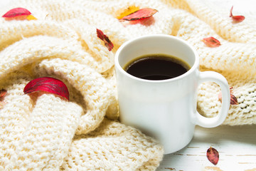 Mug of hot coffee in autumn setting on a wooden table with a knitted scarf, sweater. Comfort, warmth, cozy.