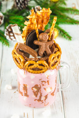 Freakshake from pink smoothie, cream. Monstershake with a chocolate man, cane, pretzels, biscuits, waffles and marshmallow. Extreme milkshake in a Mason jar. White wooden table. 