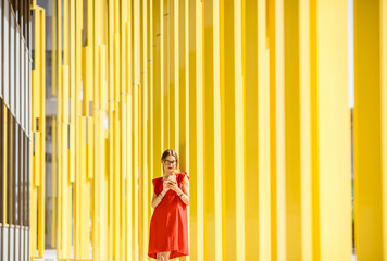 Woman in red dress using phone on the modern yellow building wall background. Abstract geometric composition