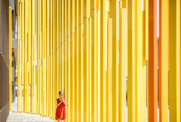 Woman in red dress on the modern yellow building wall background. General plan with abstract geometric composition