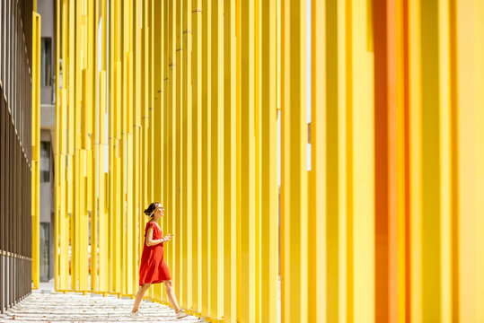 Fototapeta Woman in red dress walking on the modern yellow building wall background. General plan with abstract geometric composition