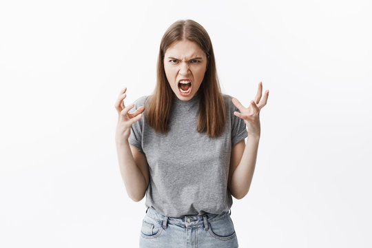 Close up portrait of mad beautiful caucasian student girl with brown hair in casual clothes looking in camera with angry face expressions, gesticulated with hands, being pissed off she broke her bew