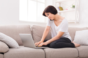 Obraz premium Pensive girl with laptop and mobile sitting on beige couch