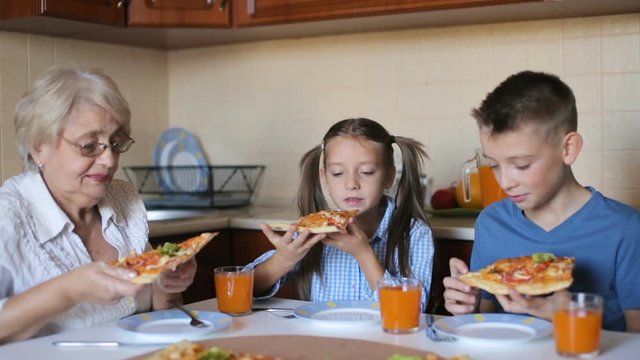 Grandmother with grandchildren are eating pizza at home
