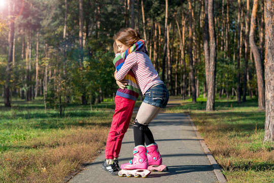 Red-haired girl on roller skates hugging boy in park.