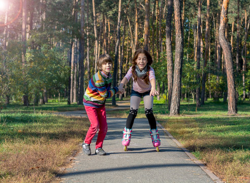 Boy helps the girl to roller-skate in the park. Brother supports his sister, who is riding on the rollers.