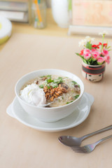 Rice porridge with garlic and egg breakfast in white bowl on wooden table