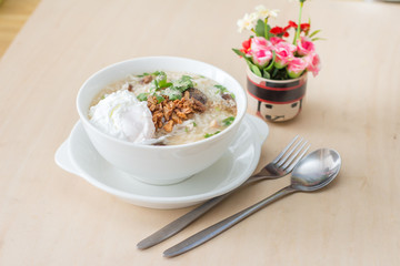 Rice porridge with garlic and egg breakfast in white bowl on wooden table