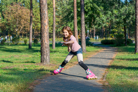 Red-haired girl with braids skates on pink rollers and falls in the park.