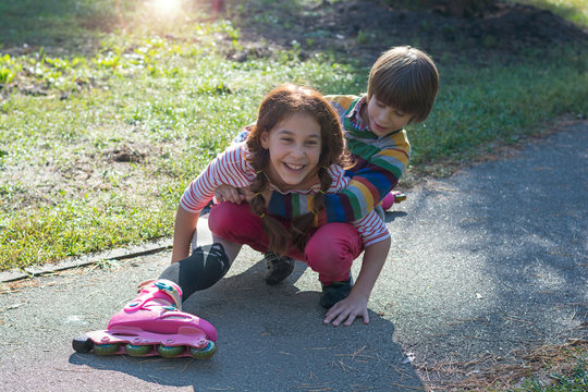 A little boy raises his sister who fell on roller skates.