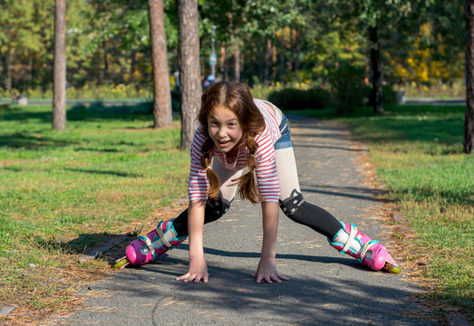 Red-haired girl with braids riding on rollers and falls in the park.