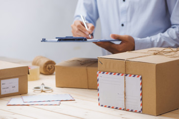Courier making notes in delivery receipt among parcels at table