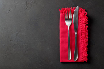 Festive set of knife and fork on a red napkin on a dark stone slate background, top view, copyspace