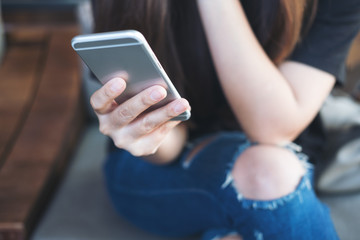 Closeup image of a woman's hand holding and using at smart phone sitting cross leg in modern cafe