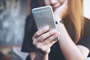 Closeup image of a beautiful Asian woman holding and using at smart phone sitting in modern cafe