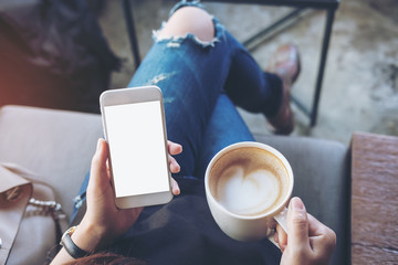 Mockup image of woman's hands holding white mobile phone with blank screen on thigh and coffee cup...