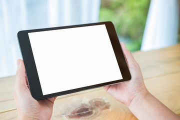 Mockup image of hands holding black tablet pc with blank white screen on wooden table in cafe