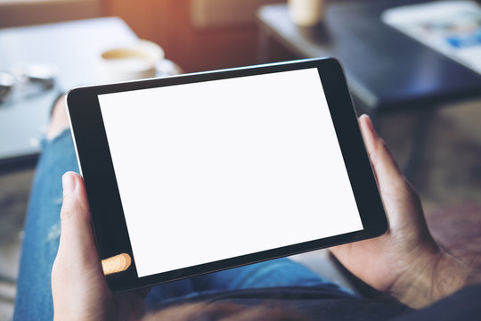 Mockup top view image of a woman sitting cross legged and holding black tablet pc with blank white screen on thigh in cafe
