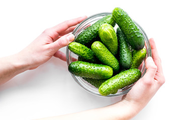 Hands take fresh cucumbers in bowl. White background top view copyspace