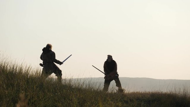 Silhouettes of two warriors Viking are fighting with swords. Contre-jour