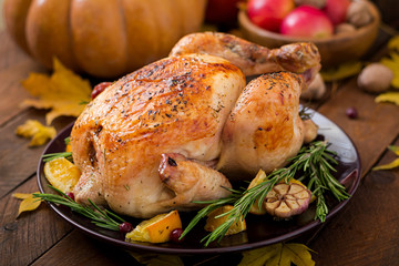 Roasted turkey garnished with cranberries on a rustic style table decorated with pumpkins, orange,...