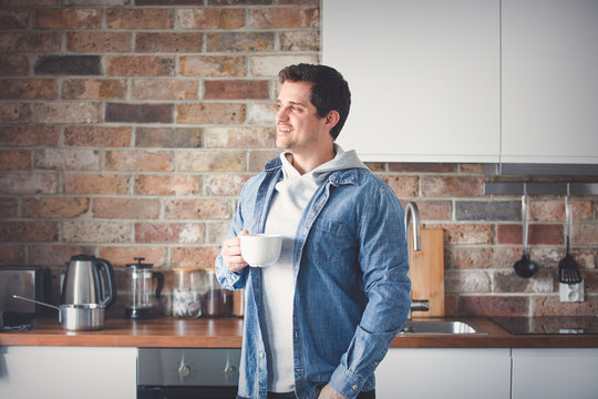 handsome man with cup of tea or coffee standing at kitchen