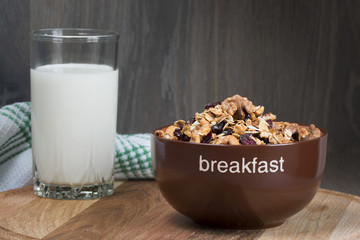 Homemade granola with honey, oatmeal, cashew nut, almond, pistachio, raisin and cranberry in clay bowl, glass with milk on wood dark table,
