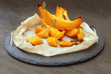 Pieces of baked pumpkin in sugar syrup on paper and black tray.