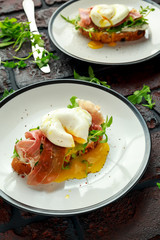 Bruschetta with cream cheese, wilde rucola, parma ham and poached egg served on white plate.
