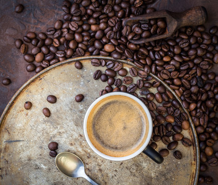 Cup of coffee on rustic steel background with coffee beans around.