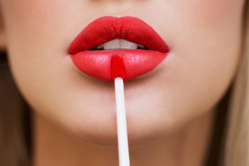 Close up portrait of attractive girl rouging her lips. She is holding red lipstick. Her mouth is...