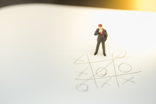 Business direction and planning concept. Businessman miniature figure standing and thinking on paper with OX (tic tac toe) board game.