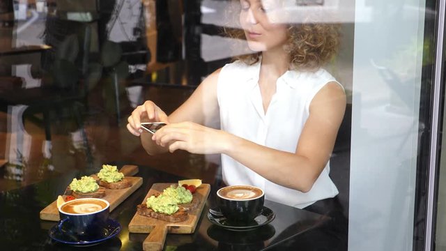 Young Business Woman Taking Picture Of Breakfast With Smartphone. Avocado Toasts And Coffee. 4K.  