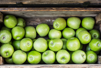fresh green apples in a wooden box on market at daytime
