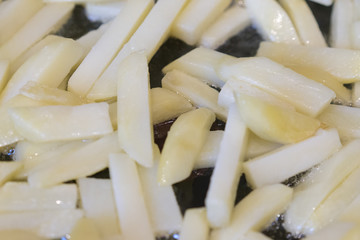 Frying rounded potatoes on a black pan with boiling oil.