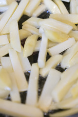 Frying rounded potatoes on a black pan with boiling oil.