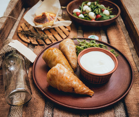 Tasty meat rolls with sour cream and salad on wooden table