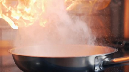 The cook sets fire to a flambe, cooking with fire, roasting and grilling, hot pan on the stove, fire in a slow motion 240 frames per second