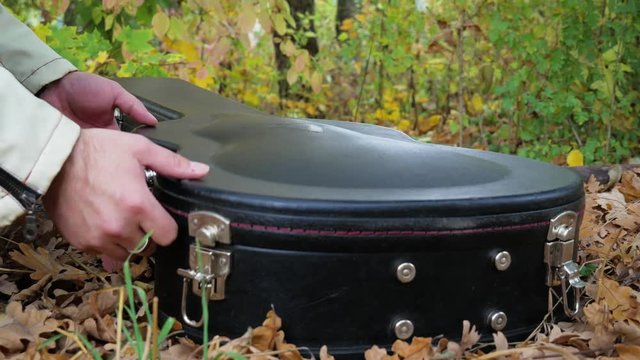 Guitarist opens coffer and take off guitar at the autumn park close-up