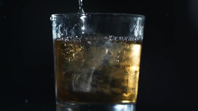 Alcohol is poured to the glass with ice cubes in slow motion, barman makes drinks, 240 frames per second