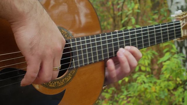 Guitar player makes music at autumn park outside close-up